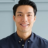 Smiling man in a blue shirt against wall.